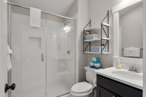 A modern bathroom with a glass shower enclosure, a toilet, a sink with a mirror, and storage shelves.
