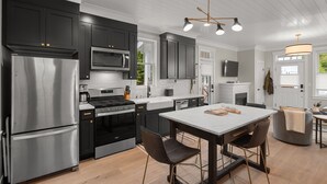 A modern kitchen with dark cabinets, stainless steel appliances, and a central island with chairs. - Seabrook Robins Nest | Pet Friendly, Hot Tub | 2BR, Sleeps 5, A/C (Pacific Beach)