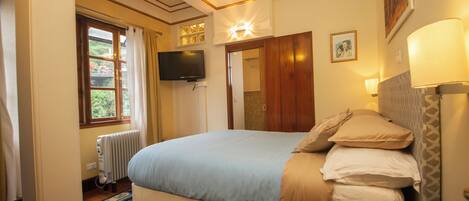 A bedroom with a bed, a television, a window with curtains, a radiator, and a bedside lamp.