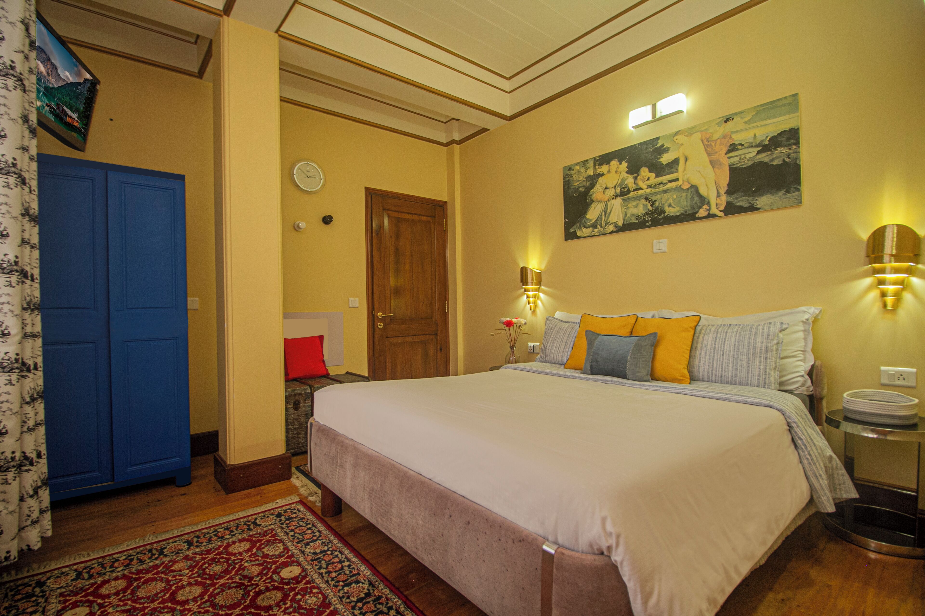 Un dormitorio bien iluminado con una cama grande, una puerta de madera, un cuadro en la pared y una mesita de noche con una lámpara.