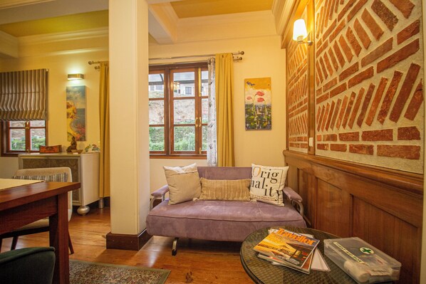 Una sala de estar acogedora con un sofá morado, una mesa de centro de madera con revistas y una pared con diseño de ladrillo.