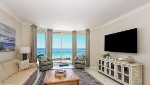 Een woonkamer met een bank, twee fauteuils, een salontafel, een televisie, een kast en een groot raam met uitzicht op de oceaan.