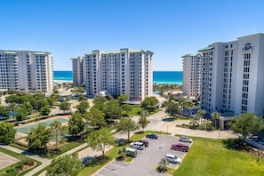 A high-rise residential building complex with multiple floors, a parking area, and a view of the ocean.
