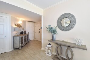 A hallway with a wooden console table, a decorative mirror, and a door leading to another room.