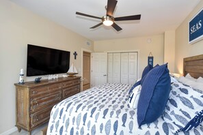 A bedroom with a bed, a dresser, a television, a ceiling fan, and a sign on the wall.
