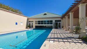 Une piscine à l’eau d’un bleu cristallin, un patio couvert et un bâtiment doté de grandes fenêtres et d’un toit végétalisé.