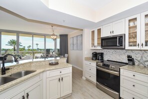 A modern kitchen with white cabinetry, a stainless steel range, and a large window overlooking a balcony with outdoor furniture.