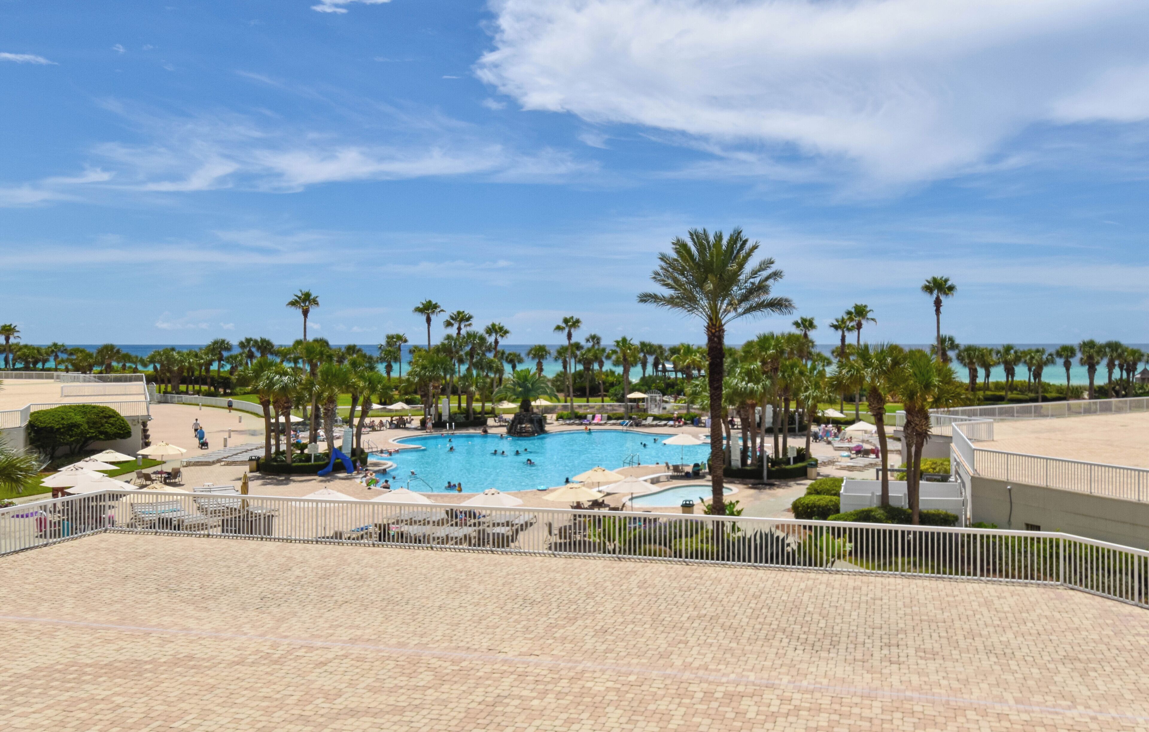 A resort with a large swimming pool surrounded by palm trees and lounge chairs.