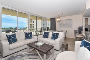 A modern living room with a sofa set, a coffee table, and a view of the ocean through large windows.