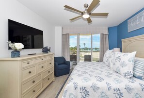 Quarto com cama, penteadeira, TV, ventilador de teto e vista para o exterior.