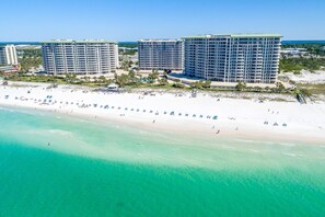 Un hotel frente a la playa con varias construcciones altas, una playa de arena y aguas turquesas cristalinas.