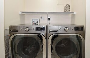 Duas máquinas de lavar roupa LG Direct Drive de abertura frontal, com painel de comandos, uma tomada e uma estante metálica acima.