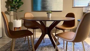 A modern dining area with a round table, four chairs, a potted plant, and a large abstract painting on the wall. - Haus of Style Moody Blues (Charlotte)