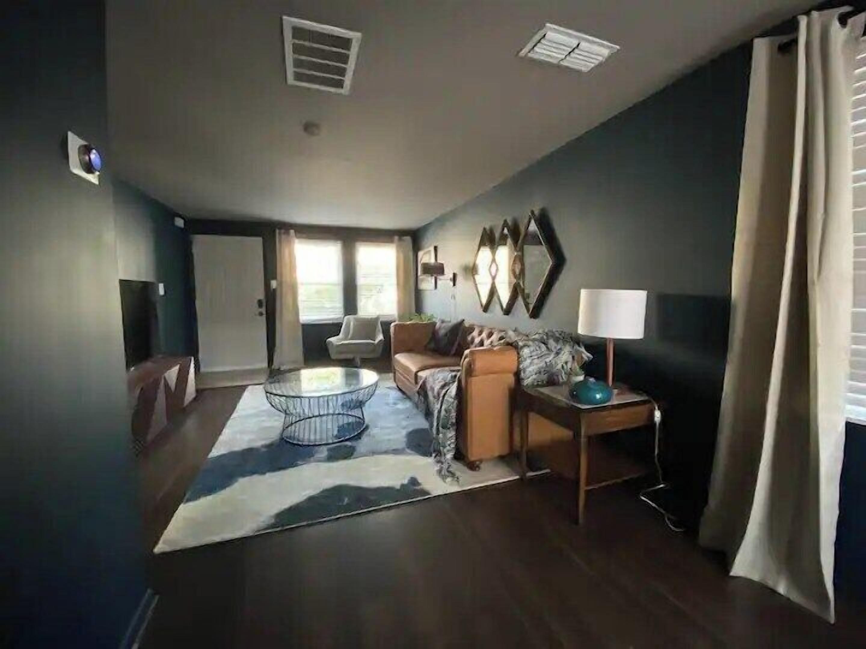 A modern living room with a glass coffee table, a sofa, a lamp, and a large window with curtains.