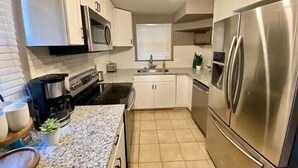 A modern kitchen with stainless steel appliances, white cabinets, and a tiled floor. - Haus of Style Moody Blues (Charlotte)
