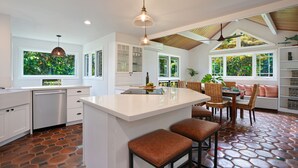 Una cocina moderna con una isla grande, armarios blancos y un comedor con mobiliario de mimbre.
