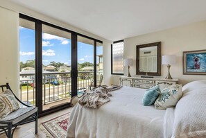 Ein Schlafzimmer mit einem großen Bett, einem Schminktisch, einem Sessel und einem Balkon mit Blick auf die Umgebung.