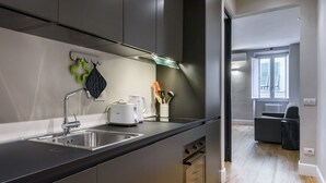 A modern kitchen with stainless steel appliances, a black countertop, and a view to the living area. - Dimora Santa Croce by Mmega (Florence)