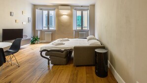A compact bedroom with a bed, a desk, and a chair. There are two windows with shutters, a radiator, and a potted plant. - Dimora Santa Croce by Mmega (Florence)