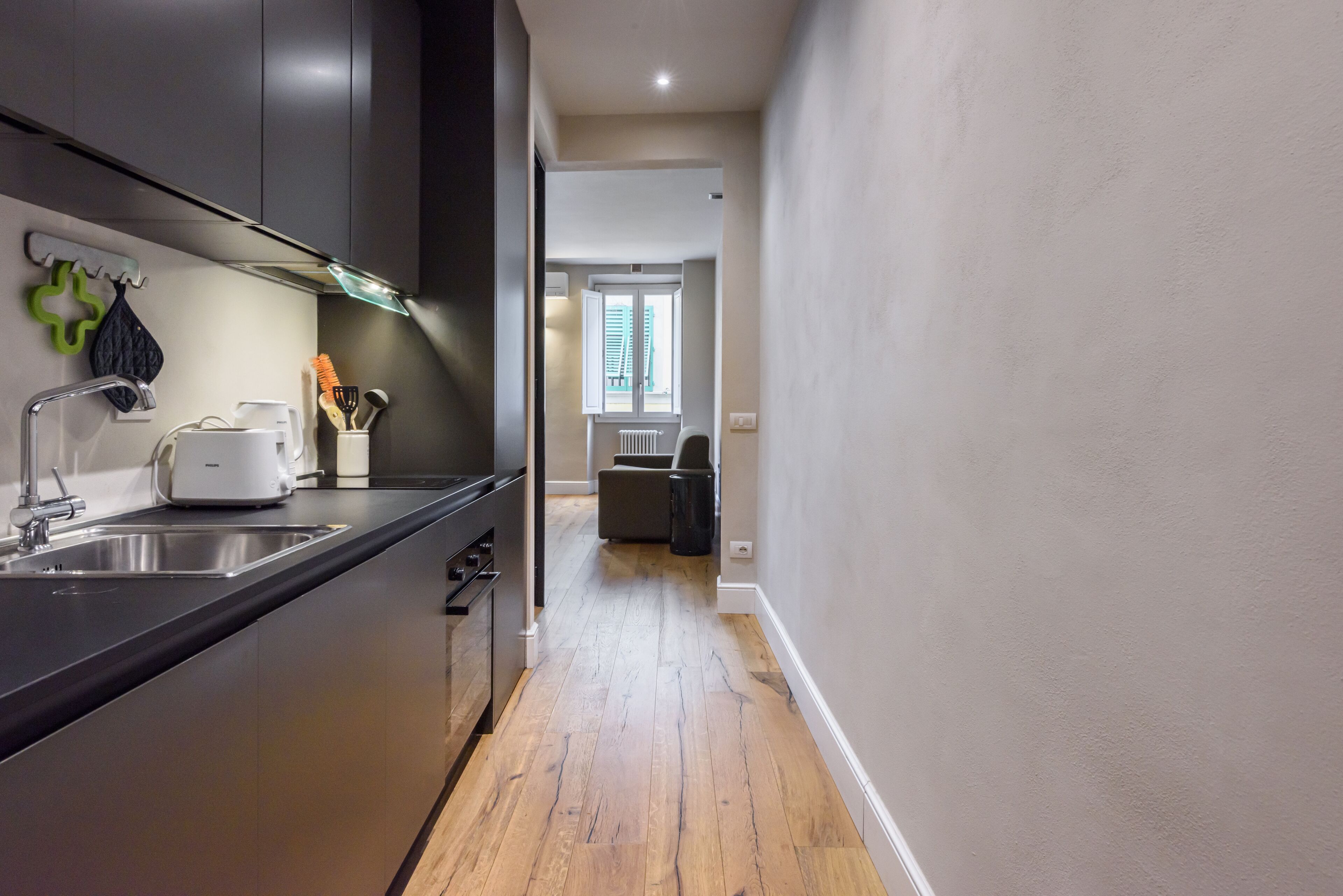 A modern kitchen with dark cabinets, a stainless steel sink, and a wooden floor.