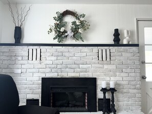 A white brick fireplace with a black mantel, a decorative wreath above it, and two black candle holders on the mantel. - Pearl on Pearl in Downtown Kingsville! (Kingsville)