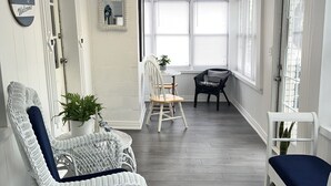 Una habitación con muebles de mimbre blancos, una mesita con una planta y una ventana con persianas.