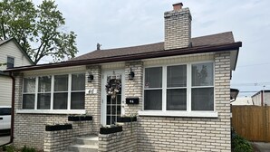 Una casa de dos pisos con fachada de ladrillo, número 46, que cuenta con un porche con escalones, una chimenea y un jardín con acolchado y plantas pequeñas.