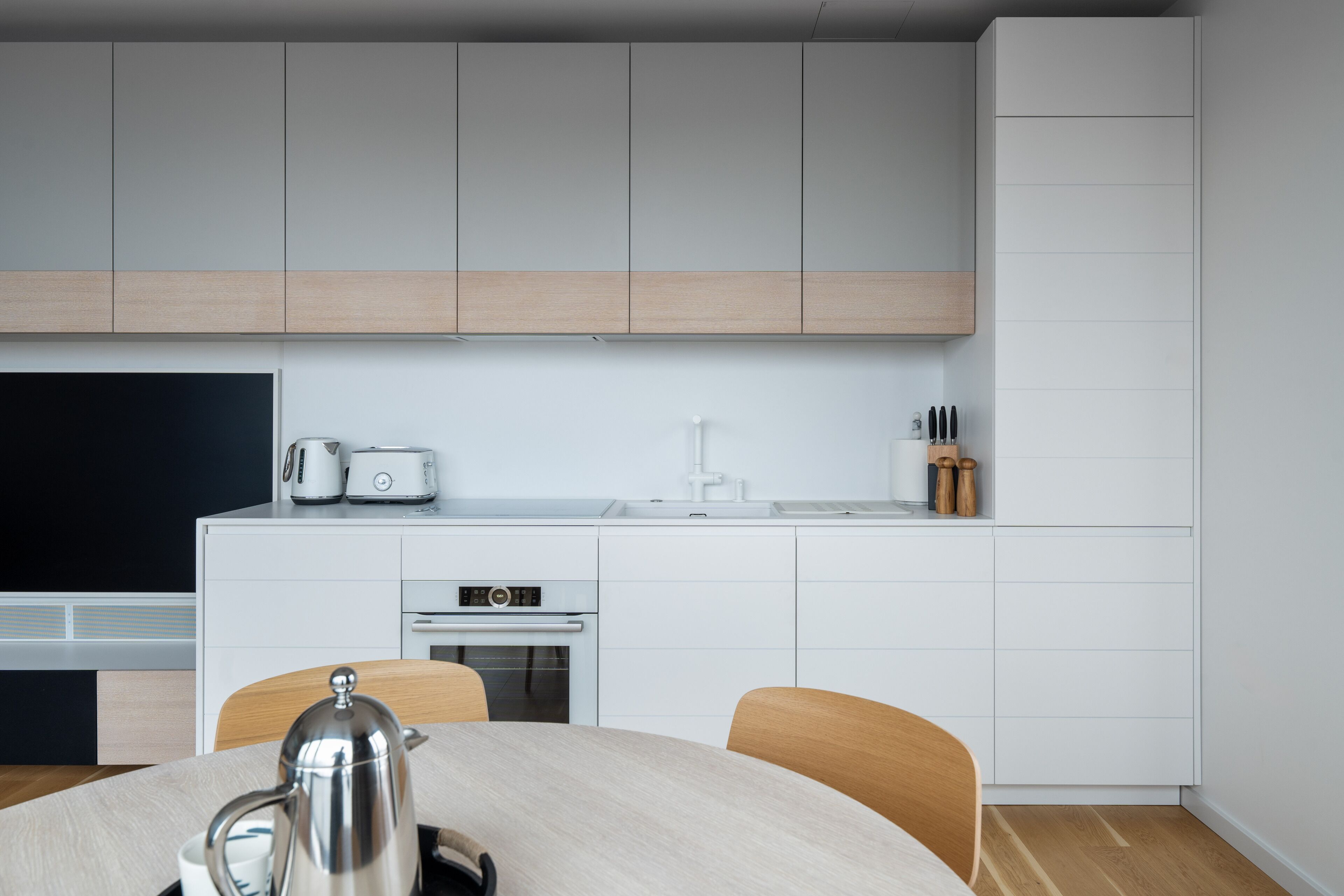 Una cocina moderna con armarios blancos, horno empotrado y un comedor con mesa y sillas.