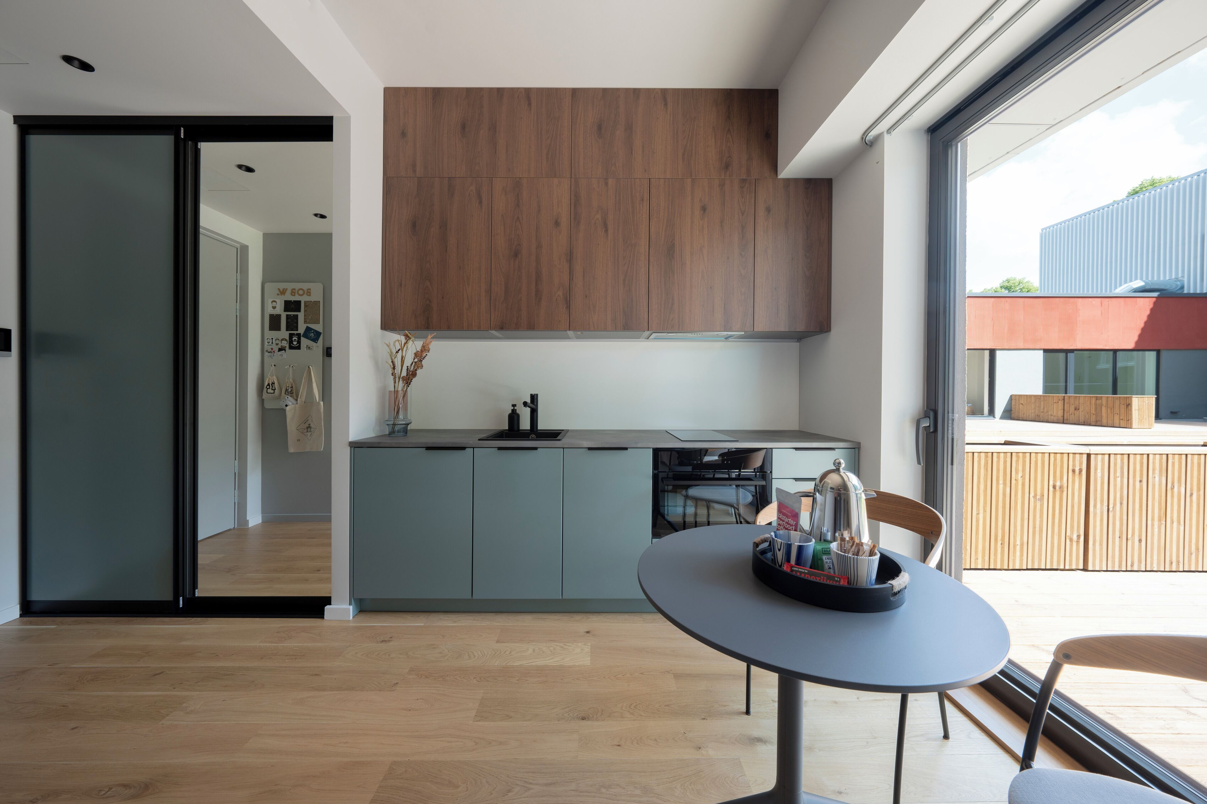 A modern kitchen with a wooden upper cabinet, a grey island, and a dining area with a table and chairs.