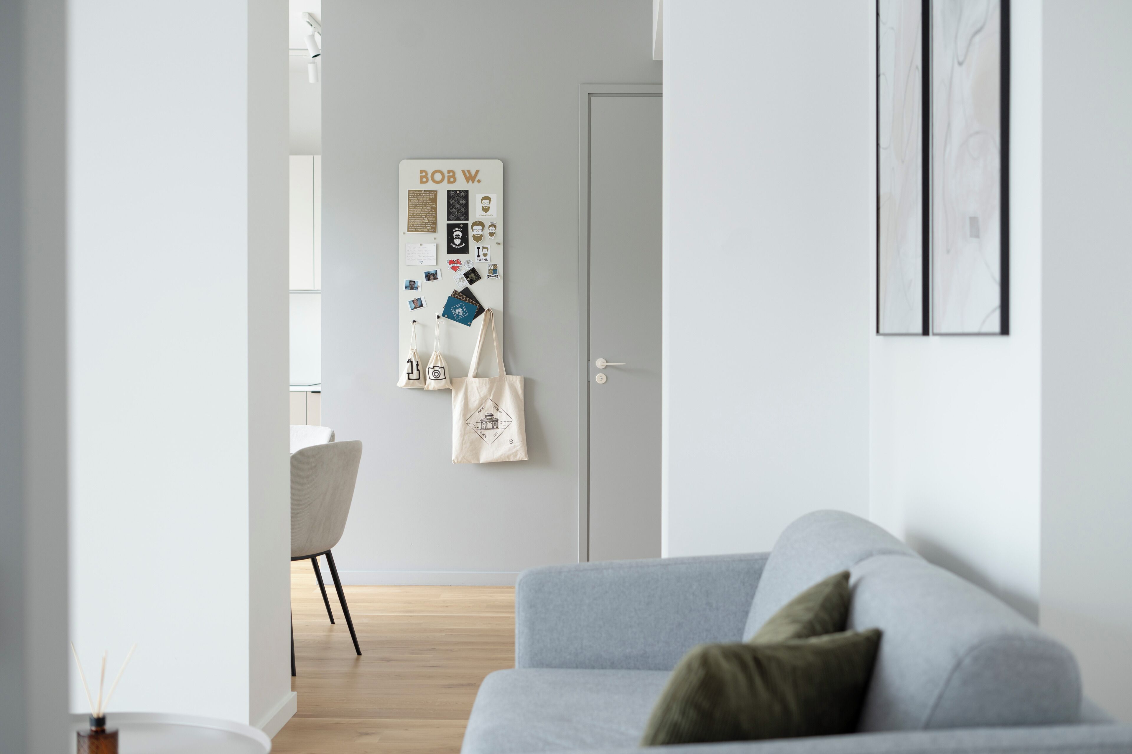 A modern living room with a grey sofa, a whiteboard with various notes and photos, a white chair, and a wooden floor.