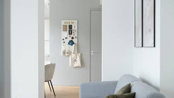 A modern living room with a grey sofa, a whiteboard with various notes and photos, a white chair, and a wooden floor.