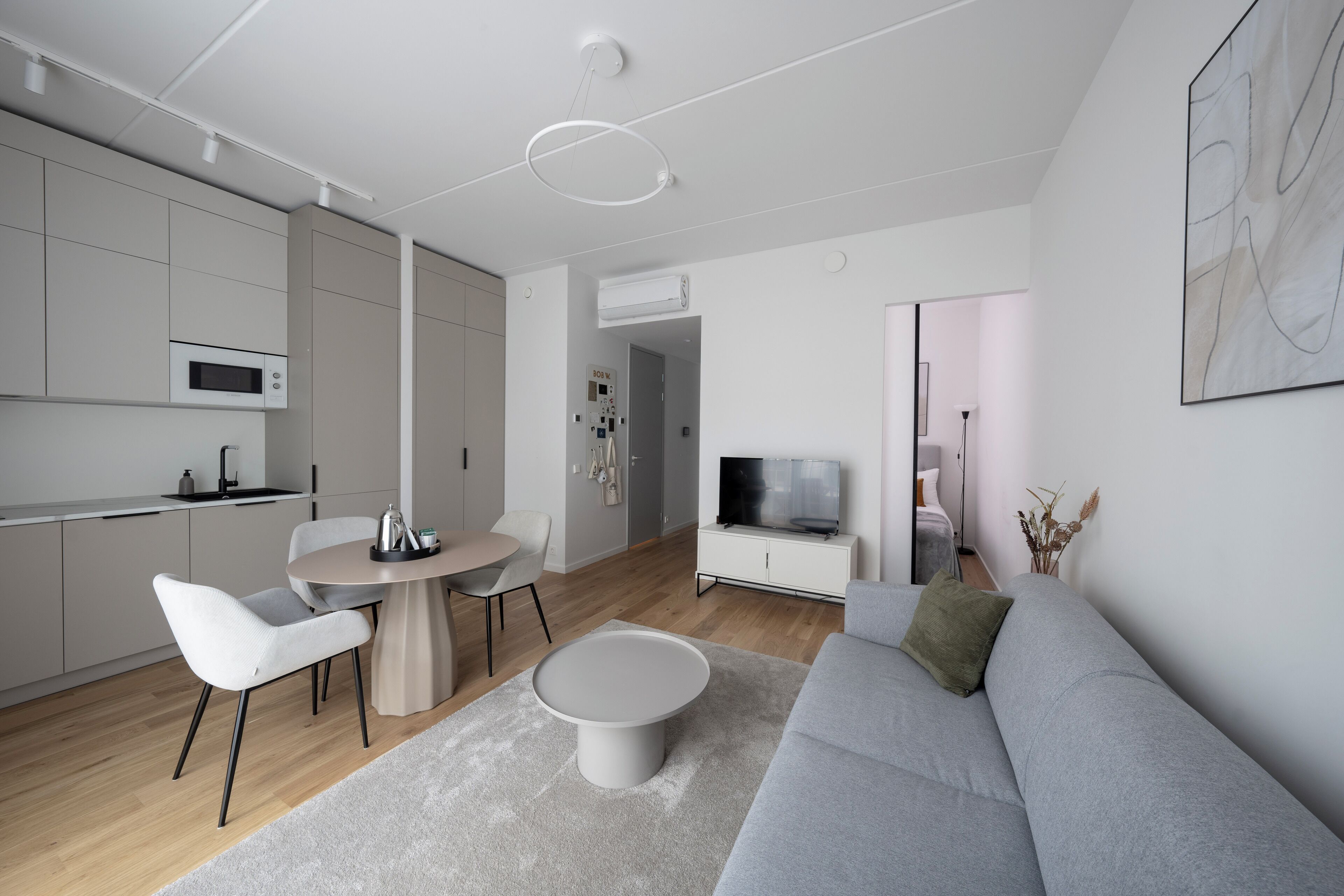 A modern living room with a grey sofa, a round coffee table, and a dining area with a small table and chairs.