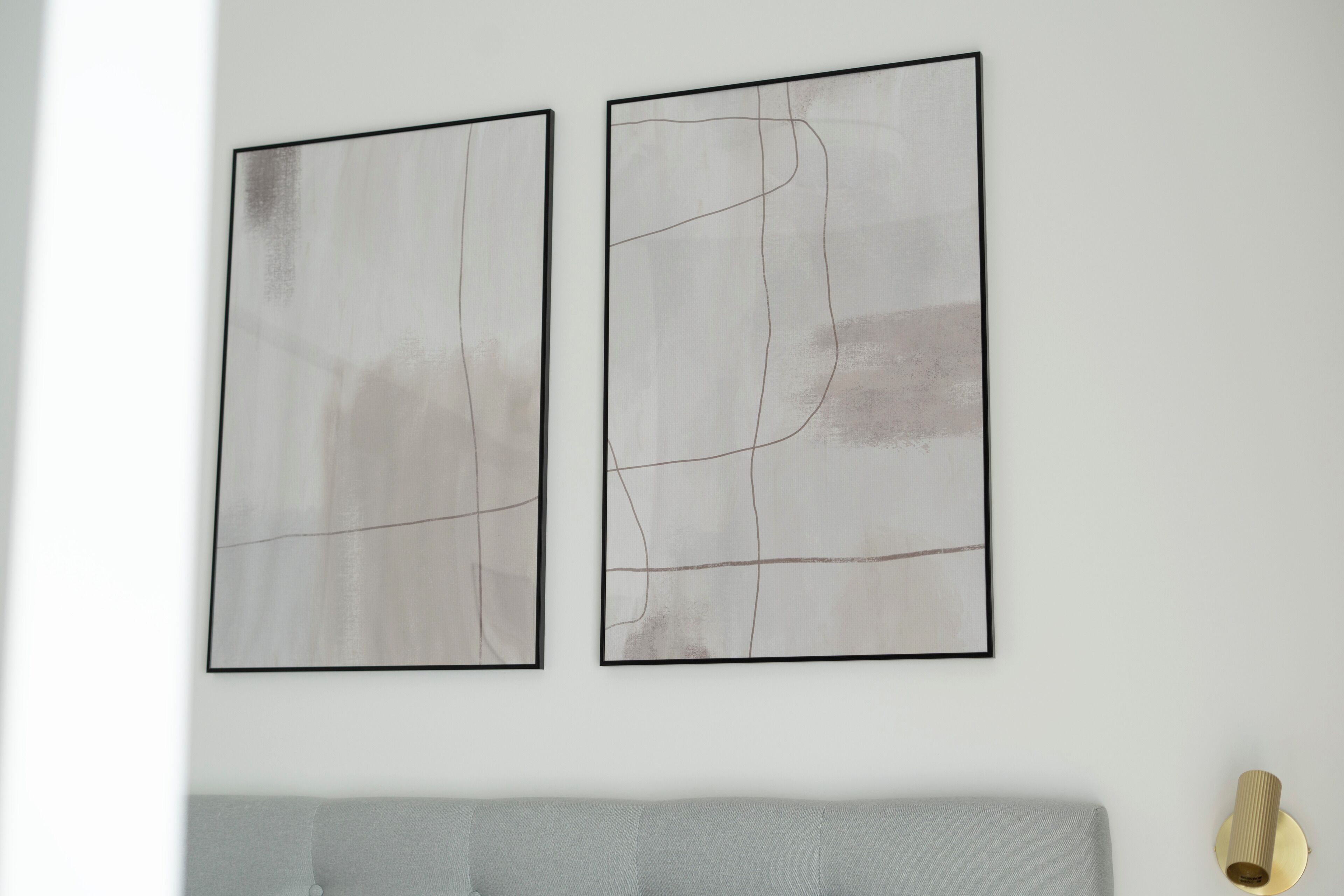 To abstrakte malerier på en hvid væg over en grå sofa.