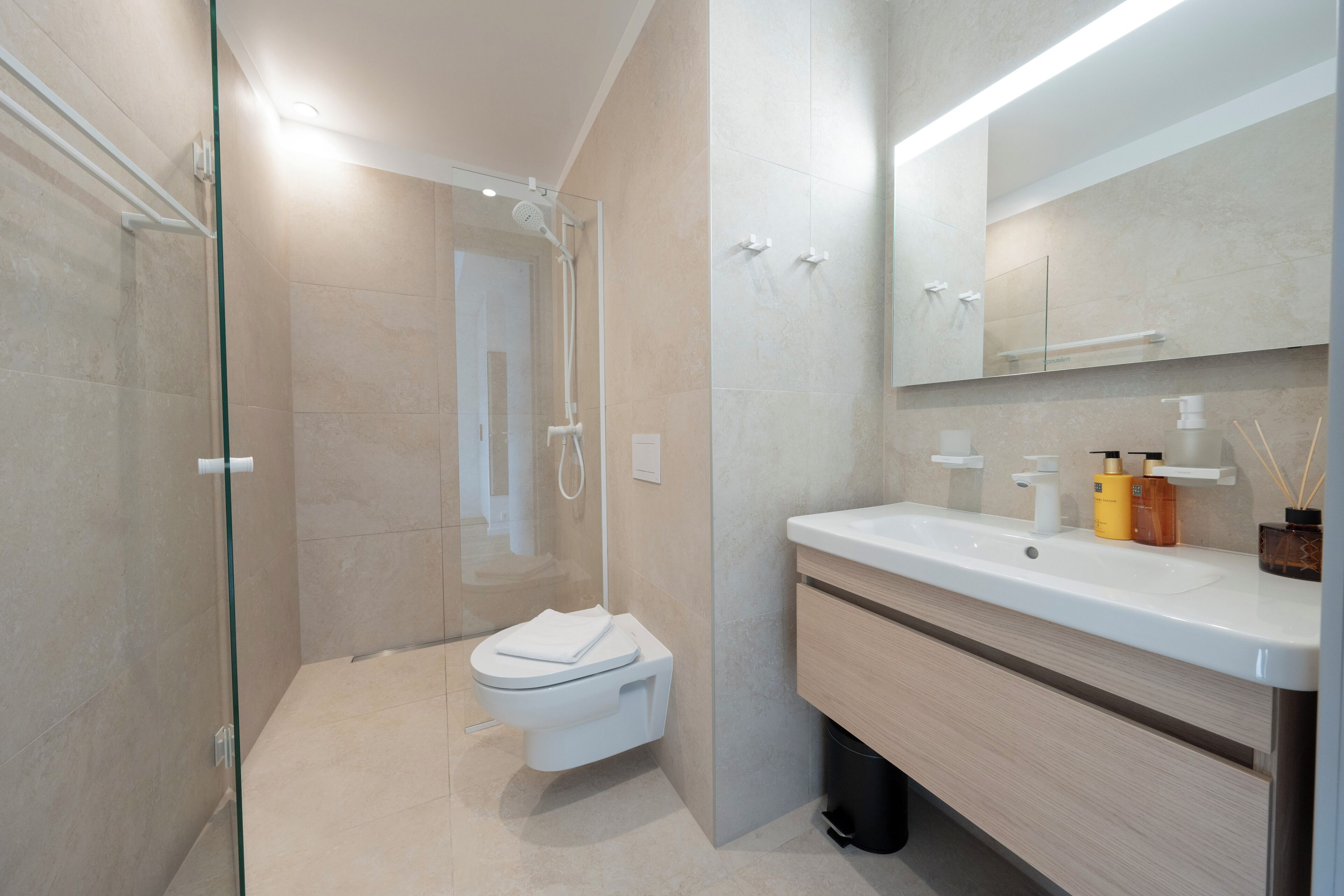 A modern bathroom with a glass shower enclosure, a white toilet, a wooden vanity with a mirror, and a sink.