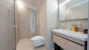 A modern bathroom with a glass shower enclosure, a white toilet, a wooden vanity with a mirror, and a sink.