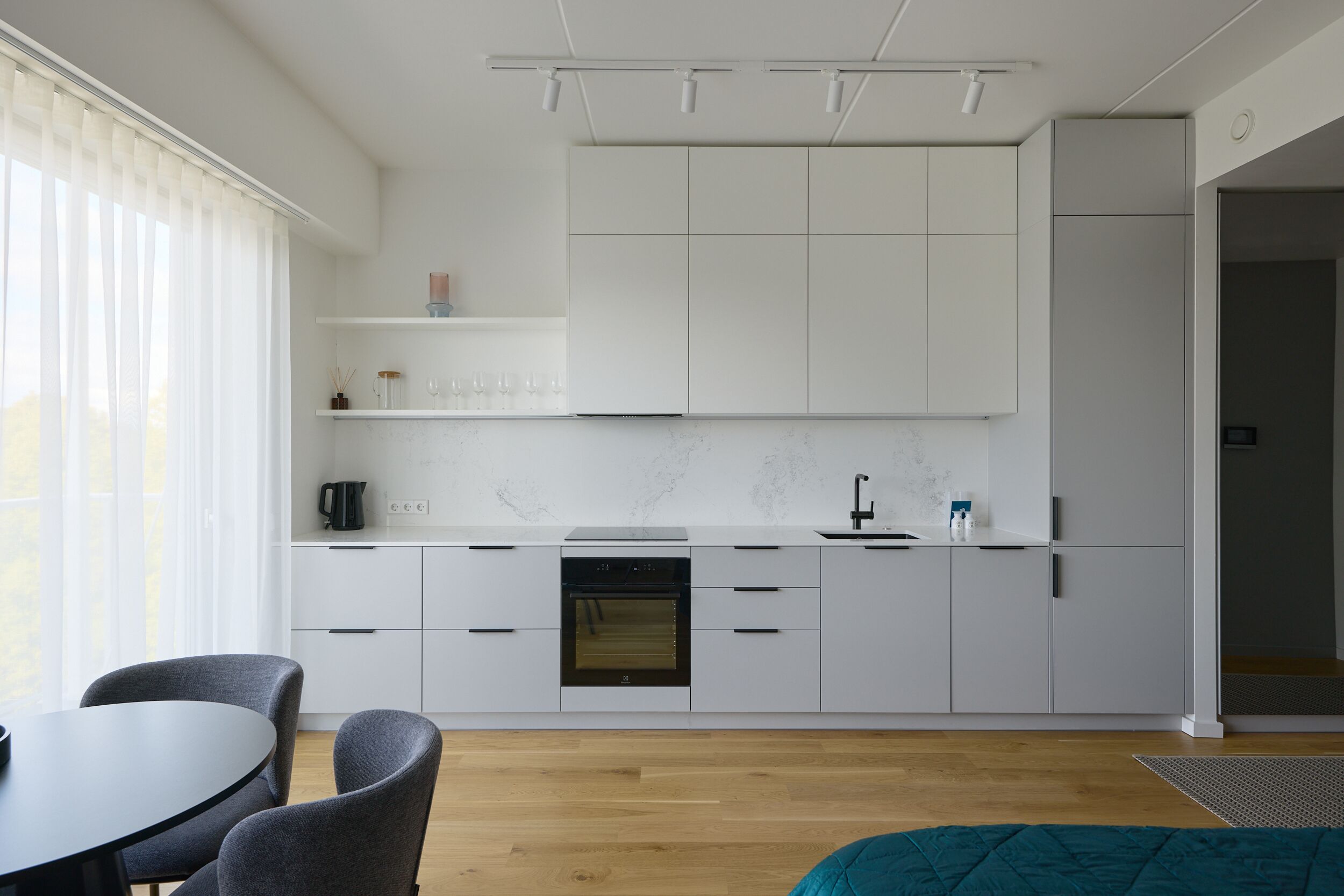 A modern kitchen with white cabinets, a built-in oven, and a dining area with a table and chairs.