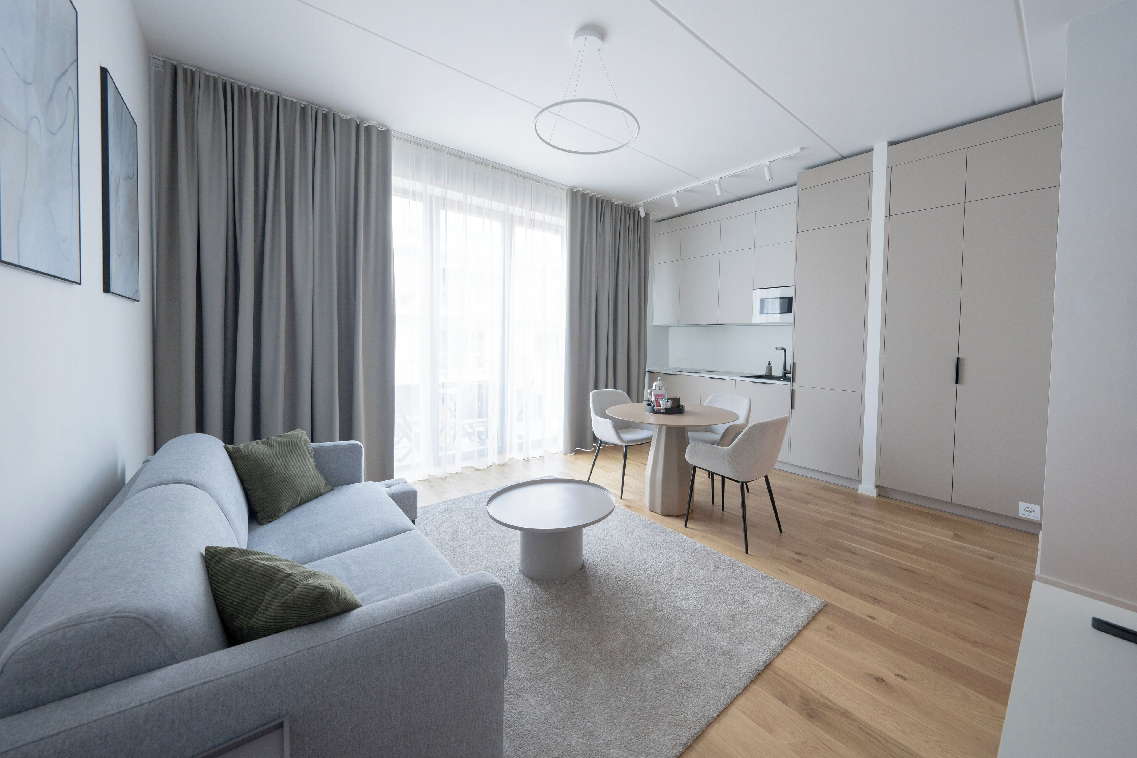 A modern living room with a grey sofa, a round coffee table, and a dining area with a small table and chairs.