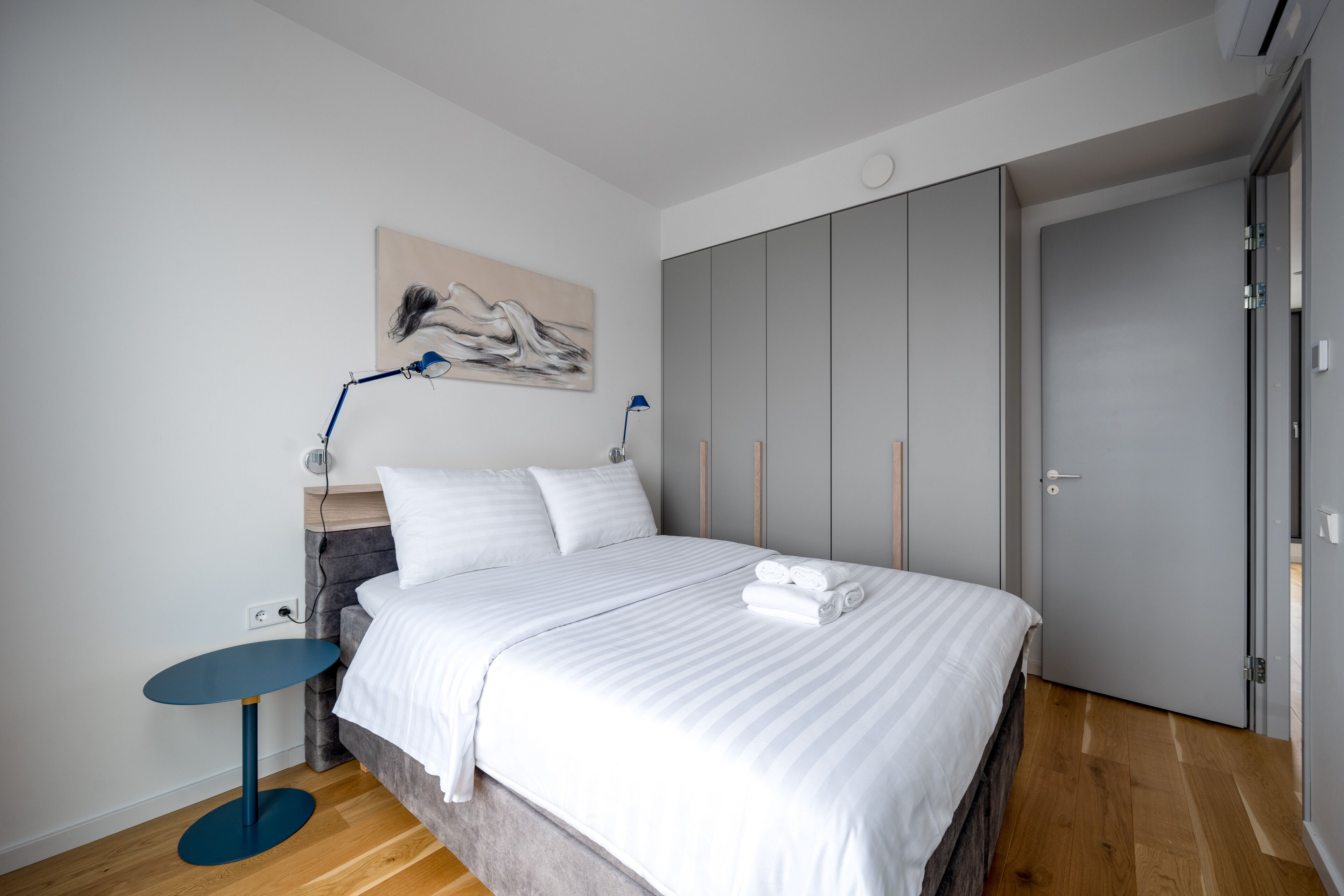 Een moderne slaapkamer met een groot bed, een nachtkastje, een lamp en een kledingkast.