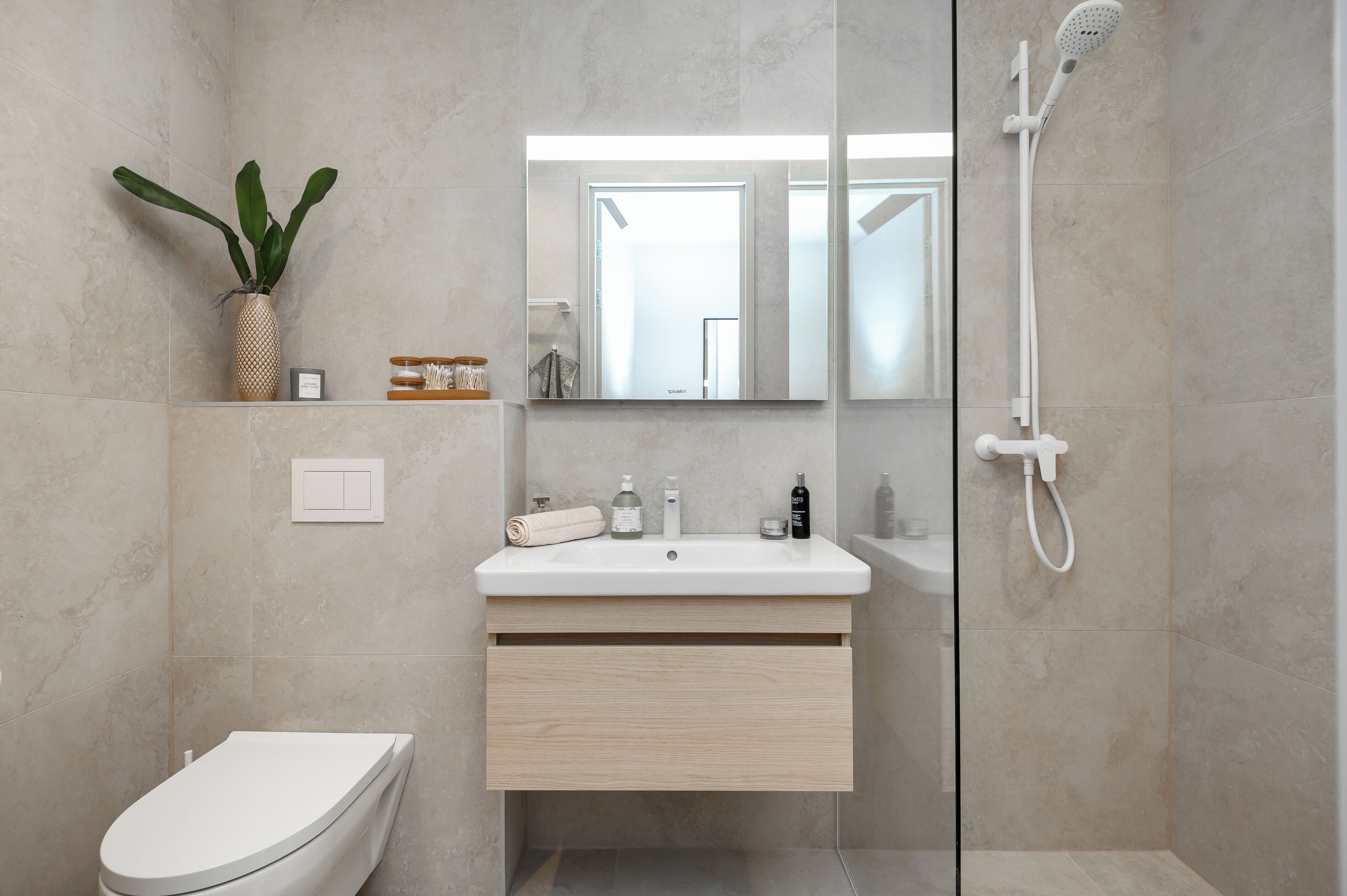 A modern bathroom with a toilet, sink, mirror, shower, and a potted plant.