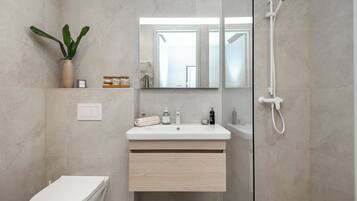 A modern bathroom with a toilet, sink, mirror, shower, and a potted plant.
