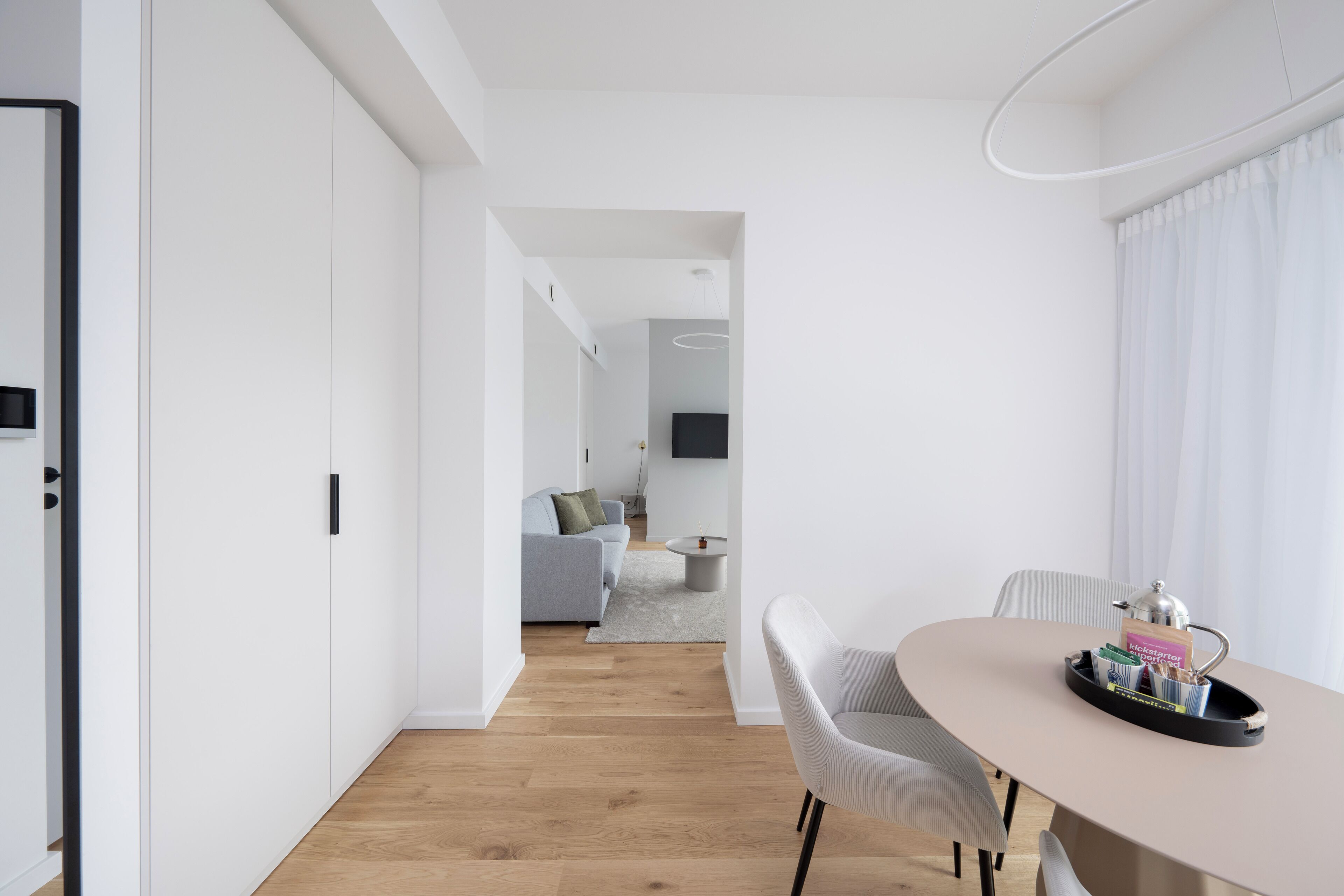 Un salón moderno y minimalista con comedor, que presenta suelo de madera, paredes blancas y muebles contemporáneos.