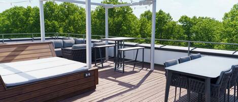 A wooden deck with outdoor seating, including a sofa and tables, under a white pergola.