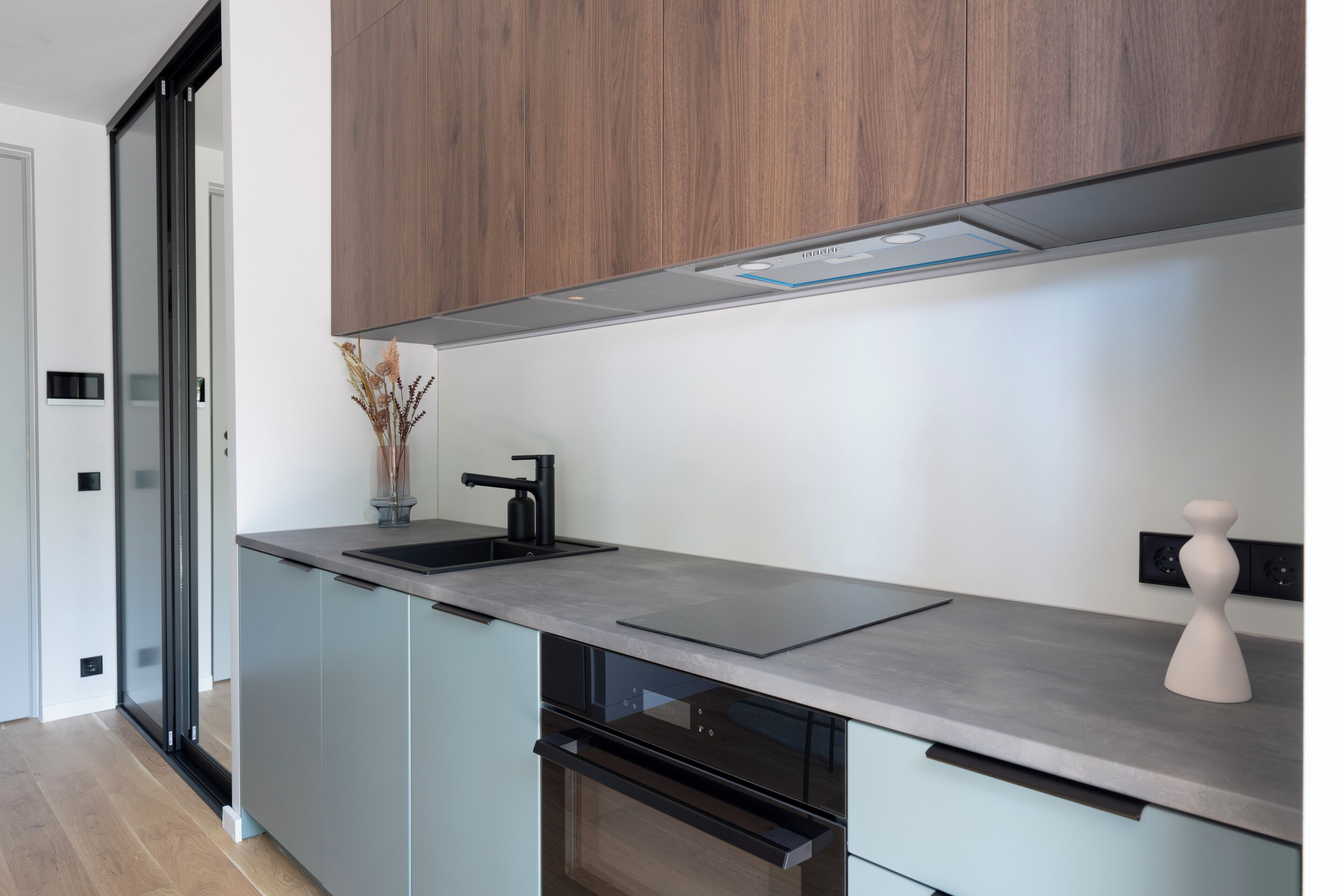 A modern kitchen with a sleek design, featuring a stainless steel sink, a built-in oven, and a wooden upper cabinet.