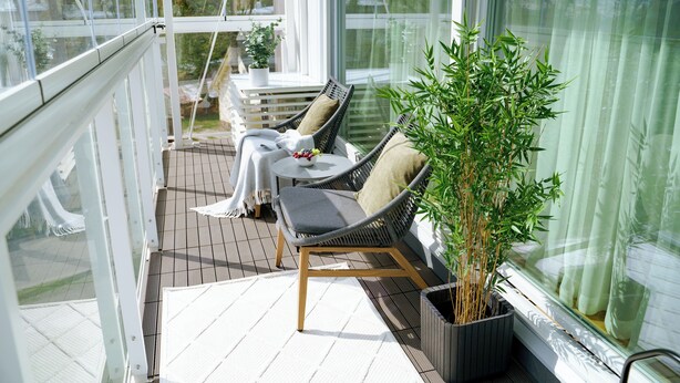 A sunlit balcony with a wicker chair, a small table, and a potted plant. - Bob W Pärnu (Parnu)