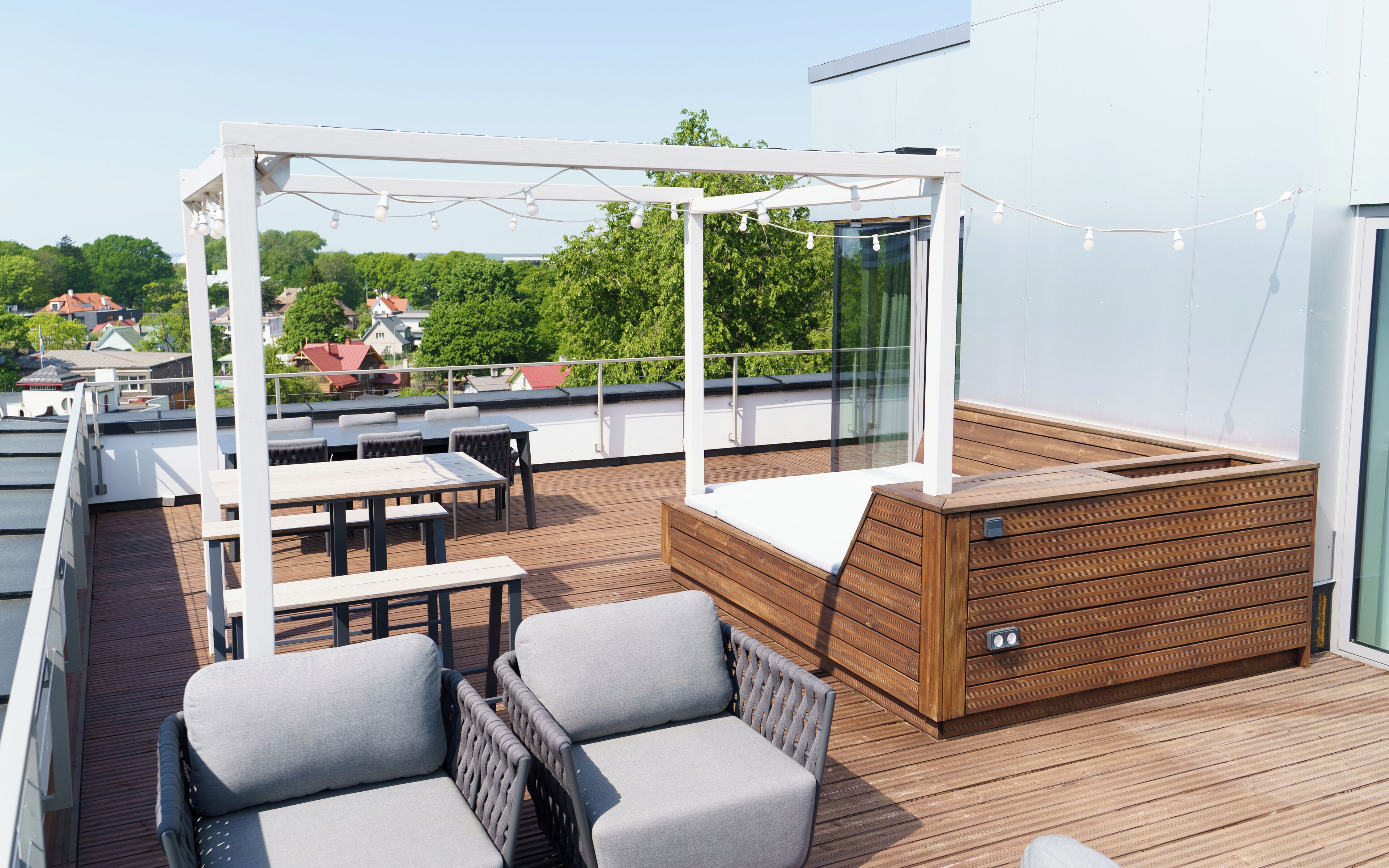 A rooftop terrace with a wooden deck, outdoor seating, and a pergola with string lights.