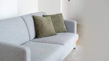 Un sofá gris con dos almohadas verdes en una habitación con paredes blancas y suelo de madera.