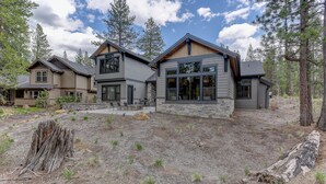 A modern two-story house with a stone foundation, large windows, and a landscaped yard with pine trees. - SABL14 - Stunning Caldera Springs, Gourmet Kitchen, Heated Patio, New Hot Tub (Sunriver)