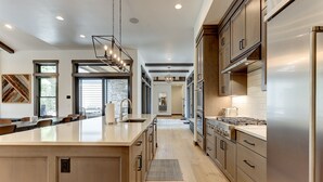 A modern kitchen with a large island, stainless steel appliances, and a view to the dining area. - SABL14 - Stunning Caldera Springs, Gourmet Kitchen, Heated Patio, New Hot Tub (Sunriver)