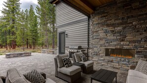 An outdoor patio with wicker furniture, a stone fireplace, and a grill. - SABL14 - Stunning Caldera Springs, Gourmet Kitchen, Heated Patio, New Hot Tub (Sunriver)
