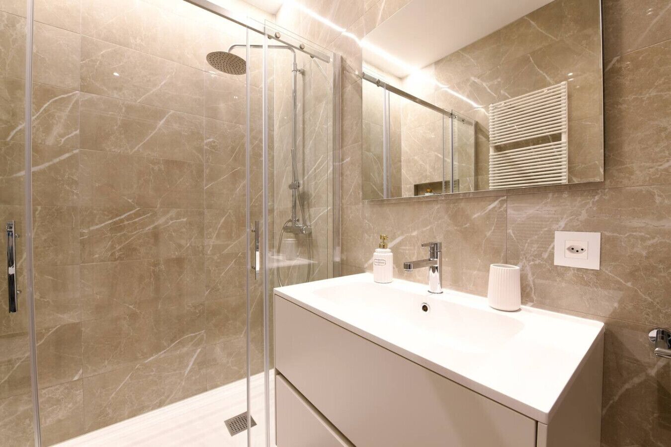 A modern bathroom with a glass-enclosed shower, a white vanity with a mirror, and marble walls.